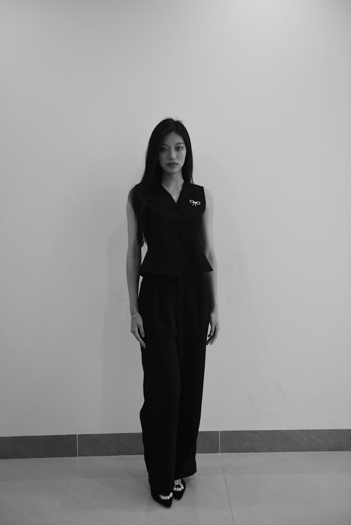 Elegant portrait of an Asian woman in black sleeveless outfit against a plain wall.