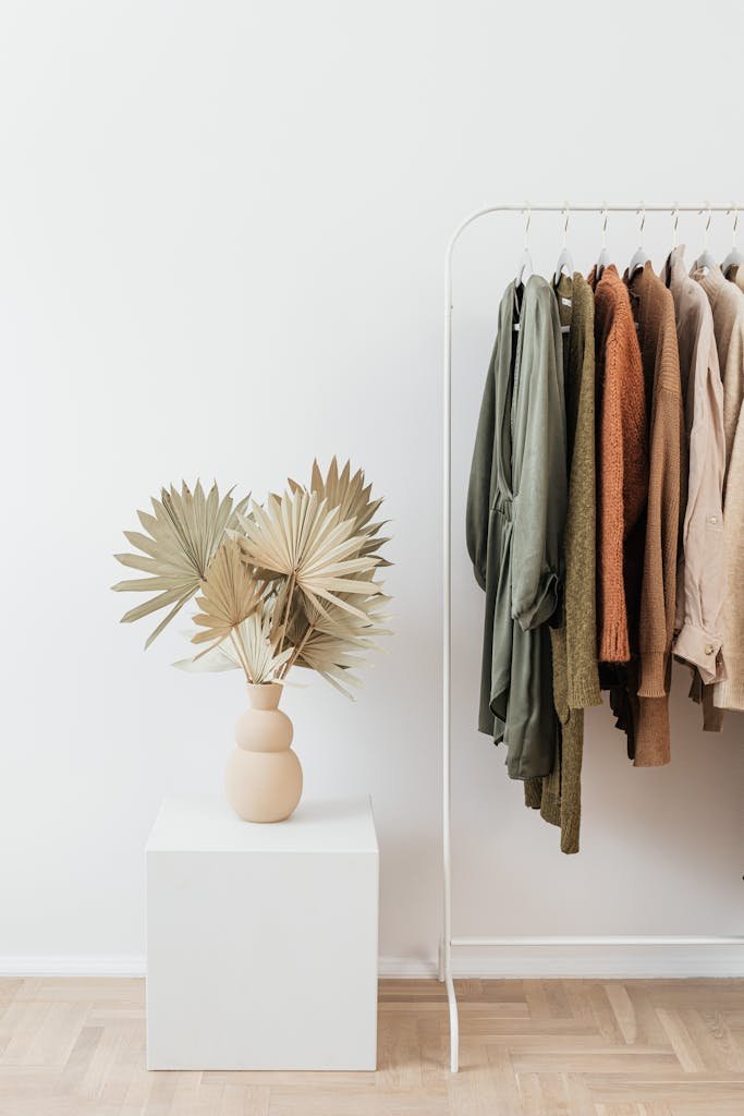 A stylish minimalist clothing display on a rack with dried palm leaves in a vase.