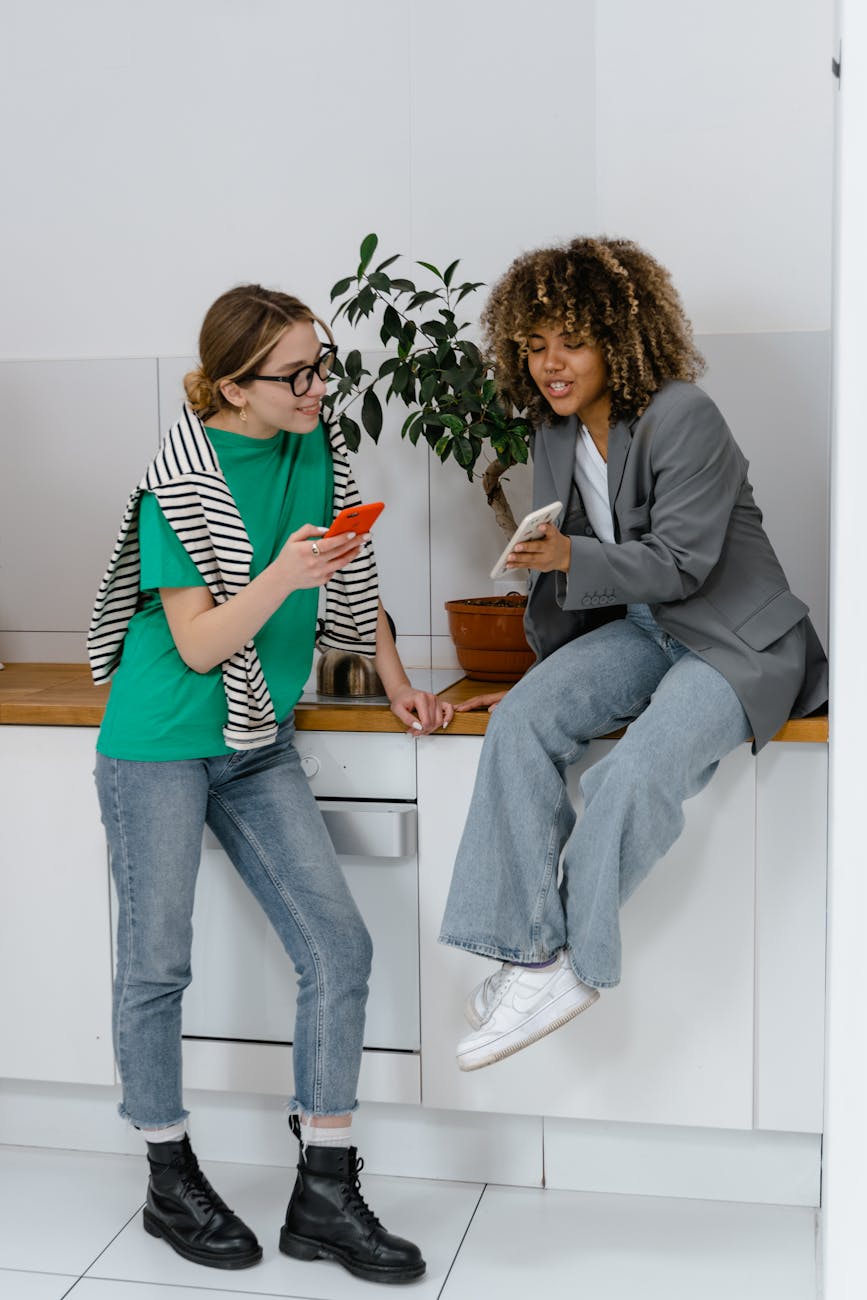 a woman in gray blazer talking to the woman in green shirt while holding their mobile phones