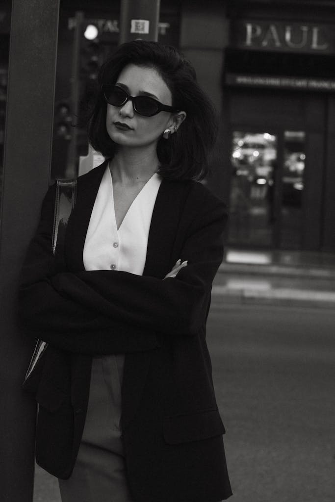 Stylish woman in sunglasses poses elegantly on city street, reflecting urban fashion.
